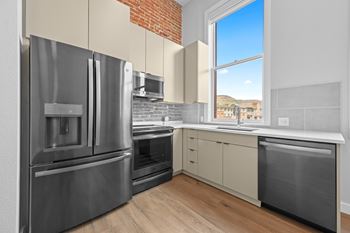 A modern kitchen with stainless steel appliances and a brick accent wall at The Avenue Lofts Golden Apartments, Golden, CO